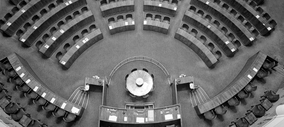 Valokuva istuntosalista, jossa näkyvät hallituksen ja virkamiesten aitiot, puhujankorokkeet sekä pikakirjoittajien pyöreä pöytä.