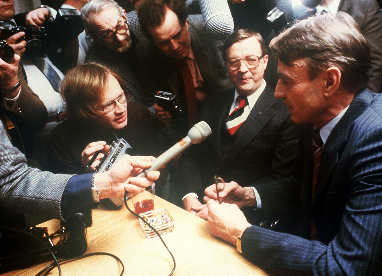 Valokuvassa SDP:n presidenttiehdokas Mauno Koivisto vastaamassa median kysymyksiin presidentin valitsijamiesvaalin ääntenlaskun jälkeen vuonna 1982. Puolueen pääjohtaja istuu tilaisuudessa Koiviston vieressä.